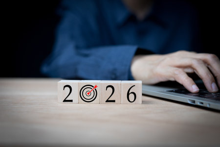 A hand uses a laptop with wooden blocks showing 2026 and a target icon, symbolizing business planning, future vision, achieving goals. project management, and successful strategies.の写真素材