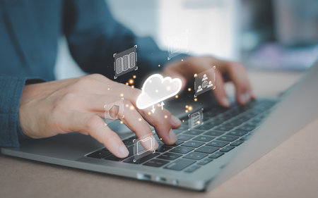 A person's hands working on a laptop keyboard, with cloud icon and various digital symbols. Concept of cloud computing, data storage, and network security. digital transformation, and online workflow.の写真素材