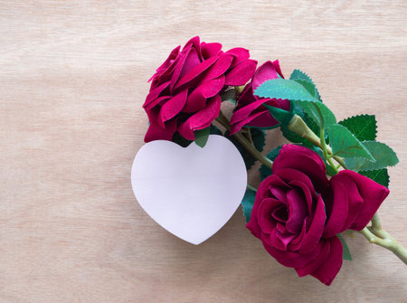 Pink heart shaped card with red roses on wooden background. Love, Anniversary, Valentine's Day card concept. Top view, flat lay with copy space.の写真素材
