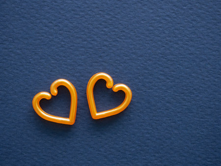 Two orange hearts are on a dark blue textured background. Concept symbolizes love, friendship, romance, and special bonds between people. Image for web banners, and social media posts. Top view.の写真素材