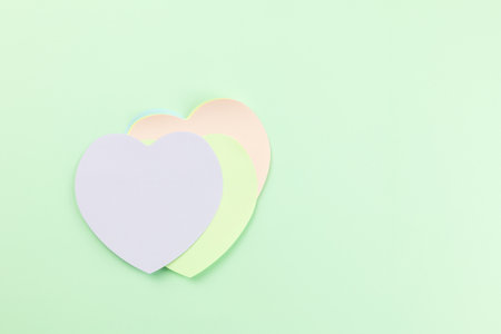 A stack of pastel heart-shaped sticky notes, purple, light green, and light pink hues, on green background. Top view, ideal for themes of love, communication, reminders, or creative projects.の写真素材