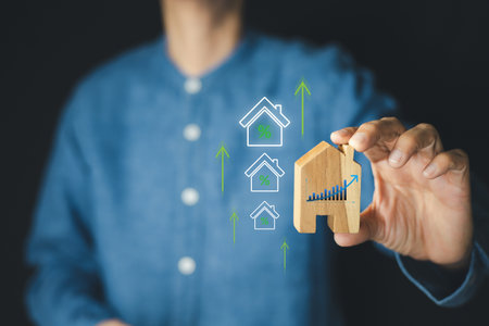 Man holding a wooden house model with graph and upward arrows overlay, real estate investment growth, property value appreciation, and financial planning success. Concept of housing market strategy.の写真素材