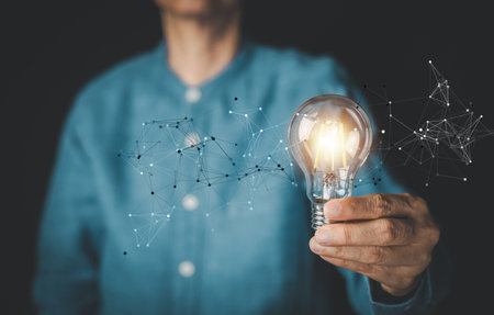 Man holding a glowing light bulb with icon network connection overlay, representing creative ideas, innovation, and digital transformation. Concept of business solution, technology, inspiration.の写真素材