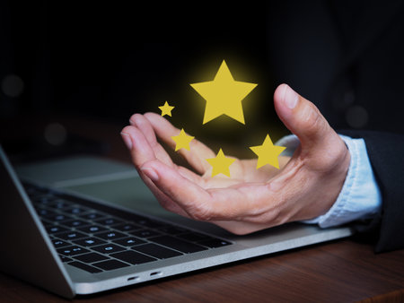 Business hand extending over a laptop to present five glowing stars, symbolizing top rating and excellent quality. Concept emphasizes customer satisfaction, positive feedback, and service excellence.の写真素材