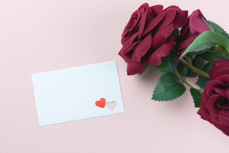 Top view, flat lay blank card with heart cutouts and deep red roses on pink background, perfect for love notes, romance, and special occasions.の写真素材