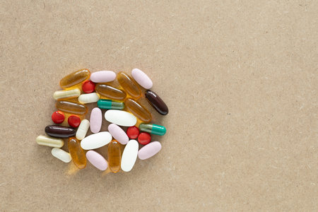Top view with copy space of assorted supplement pills and capsules on a light brown wooden background. Health insurance, and minimal medical concept.の写真素材