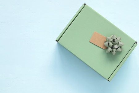 Top view flat lay of a simple green gift box with a silver glitter bow and blank craft tag. Minimalist present on a light blue wooden background. Concept for holiday, birthday, or celebration.の写真素材