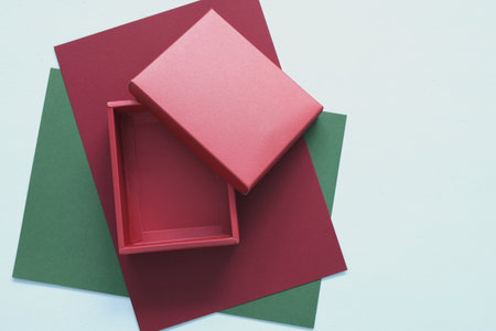 Opened empty red gift box on red and green paper sheets isolated on light blue wooden background. Top view flat lay of Christmas holiday surprise or mockup concept with copy space inside.の写真素材