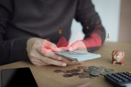 Hands counting dollar bills with a downward red trend graph overlay. Concept of financial risk,...