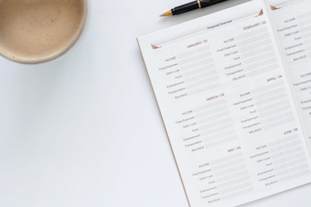 Financial planning concept with monthly budget planner notebook, pen, and coffee cup on white desk. Top view personal finance management and investment goals for saving money and wealth success.の写真素材