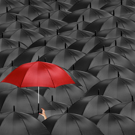 A red umbrella in the midst of many black umbrellasの写真素材