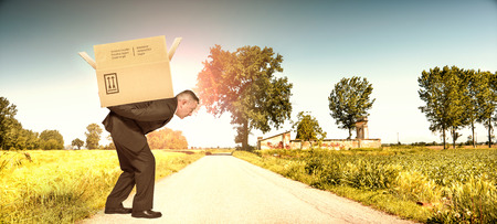 Businessman carrying heavy cardboard box on backの写真素材