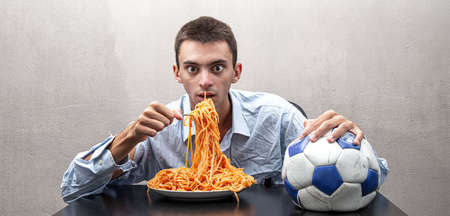 an young man eating spaghetti caught in footballの写真素材