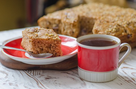Cup of hot tea and piece of honey cake on red saucer. Rustic style.