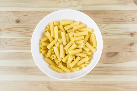 Top view of raw uncooked tortiglioni pasta in white bowl on wood tableの写真素材