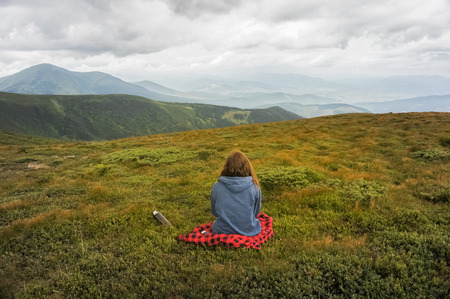 Girl sitting and enjoying beautiful view of mountain landscape on a cloudy dayの写真素材