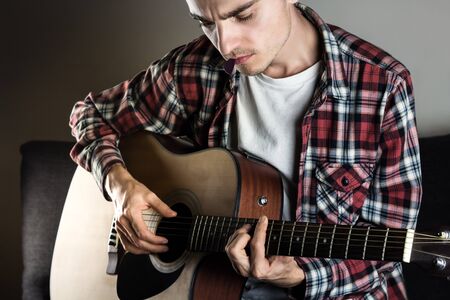 Male musician in casual wear plays acoustic instrument and holds pick in mouth