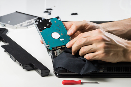 Cleaning computer hardware with cloth. Person performs service maintenance of hard disc of portable PC after dismantling it on white tableの写真素材