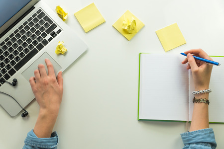 Minimalistic home office work place with laptop and note pad. Top view human hands work at desk with...