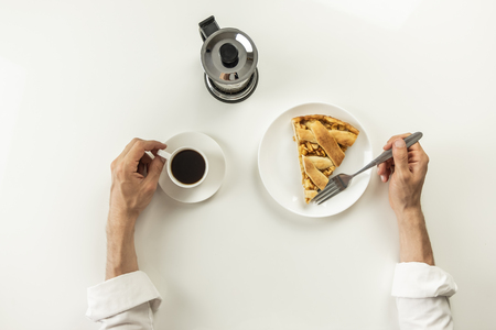 Top view of minimalistic table with business lunch with coffee, cereal and applie pie. Male hands holding cup of black coffee and fork having breakfast with granola snack and piece of cake.の写真素材