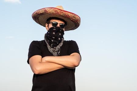 Young male person dressed up as gangster in traditional sombrero, bandana. Mexican festive or halloween concept of man posing as bandit or western style banditの写真素材