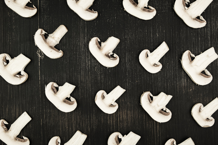 White sliced mushrooms on black wood rustic background, top view. Flat lay pattern of white champignons on tableの写真素材