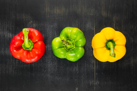 Top view of three fresh bright bell peppers on black rustic background. Shot from above of green, yellow and red paprika vegetables on dark wood tableの写真素材