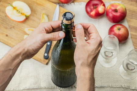 Top view of male hands opening bottle of premium cidre. Shot from above of uncorking beautiful ice cold bottle of apple wine, locally grown ripe apples in backgroundの写真素材