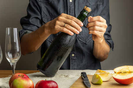 Male hands opening bottle of premium cidre. Uncorking beautiful ice cold bottle of apple wine, with ripe apples in backgroundの写真素材