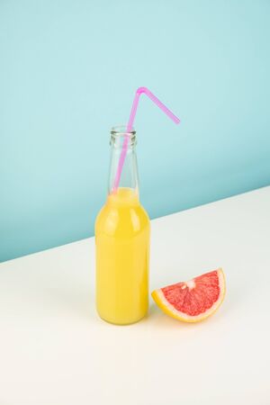 Orange drink and slice of grapefruit on white and blue background. Minimalistic image of citrus juice bottle and fruit at sparse bright environment.の写真素材