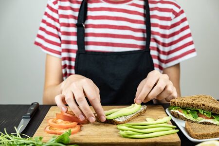Making raw food sandwich. Female hands placing slices of avocado on breadの写真素材