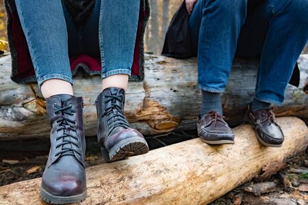 Sitting on wood logs in the forest. Close-up of female and man legs in boots in natural outdoors...