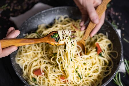 Serving traditional  italian pasta from a pan, top view. Male hands taking spaghetti in spoon and...