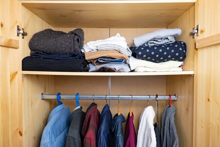 Wardrobe shelf with abundance of clothes. Consumerism concept: organised and layered personal things...