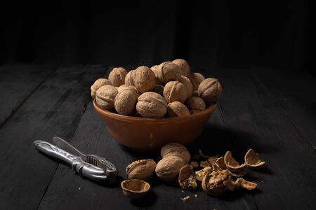 Walnuts in a bowl on dark background. Low-key image of nuts on black rustic table, artistic light...