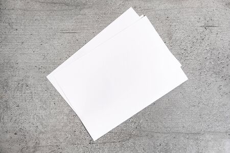 Blank paper sheets on grey background. Top view of white paper laying on cement stylised table top