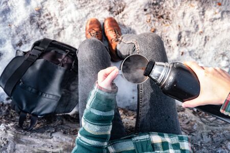 Pouring hot drink out of thermos at a campsite. Person in a winter forest during a hiking trip getting warm, point of view shotの写真素材