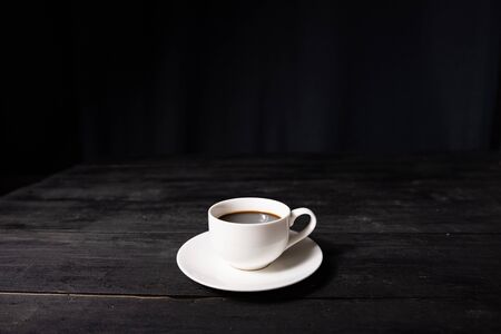 Cup of espresso coffee on vintage black table, front view. Coffee in white cup on dark background...