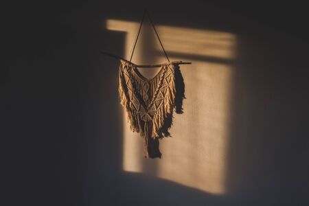 Macrame wall hanging in the sunny spot of the room. DIY boho wall tapestry hanging on the wall in the morning sunの写真素材