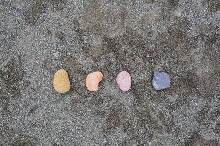 Multi-colored pebbles on wet gray sand. Yellow, orange, pink and purple pebbles on the sea beach, concept of naturalness, simplicity and beauty of nature.の写真素材