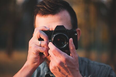 Man taking a photo with a vintage camera. Portrait of a photographer in an autumn outdoor environmentの写真素材