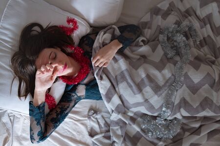Waking up after a big party. Woman in bed lit by morning light from the window, concept of hangover and sleeping after excessive partyingの写真素材