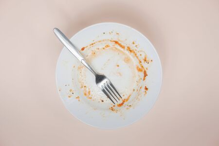 A plate with rests of tomato sauce in it, top view. Unwashed dishes illusatration, filthy plate on light backgroundの写真素材