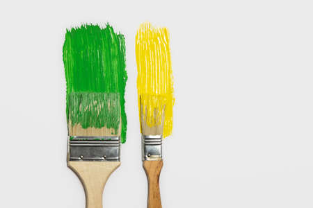 Paintbrushes and a trail of green and yellow paint in isolated background. Concept of painting, renovation, home and household choresの写真素材