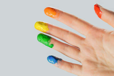 Close-up view of a hand with paint on the fingertips. Blue, green, yellow, orange and red paints on fingers, studio shot.の写真素材