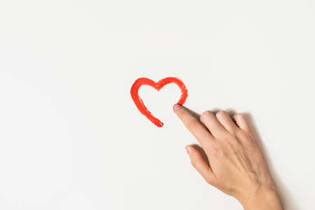Finger draws a heart's shape with red paint on a white background. Charity, love or St. Valentines day concept.の写真素材