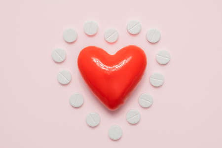 Heart and pills in the shape of a heart on pink background, top view. Cardiology, heart disease...