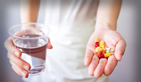 Hands with pills and glass of water isolated on whiteの写真素材