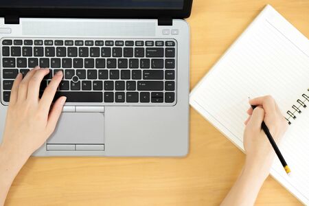 A women hands using laptop with blank screen and writing in notepad