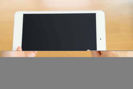 woman's hand holding a tablet on the background of a wooden tabletop